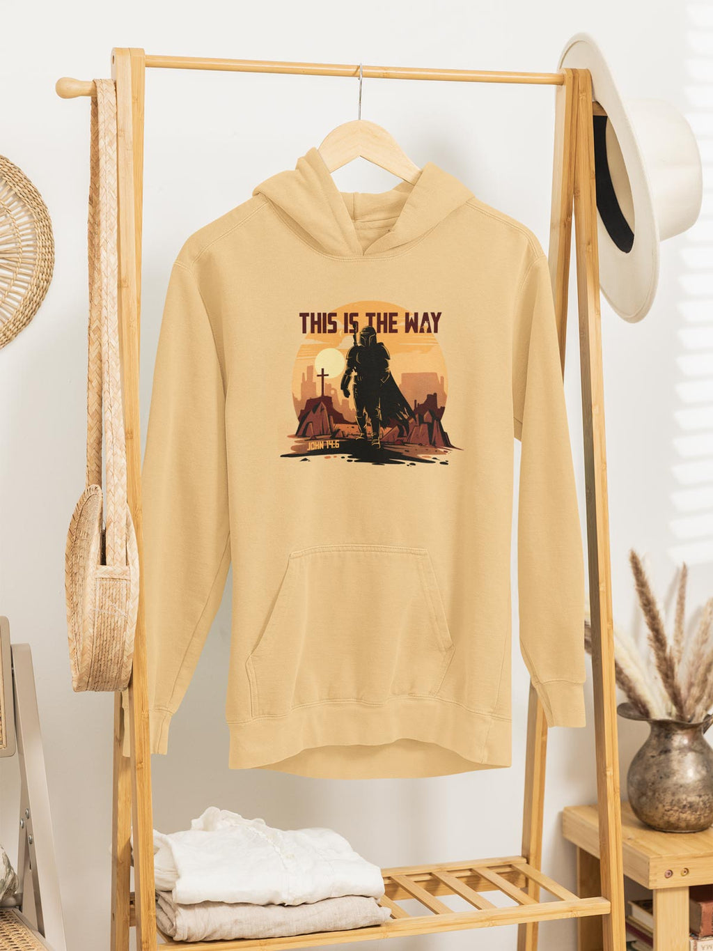 Beige hoodie with graphic design hanging on a wooden rack.
